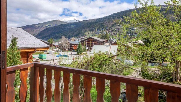 A wooden balcony overlooking a village with buildings and a mountain in the background.