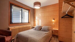 A bedroom with a bed, a radiator, a window with blinds, a hanging light fixture, and a wooden wardrobe. - 100m from ski slopes, Ground floor, terrace, parking, tv, ski locker, 67m², Morzine (Morzine)