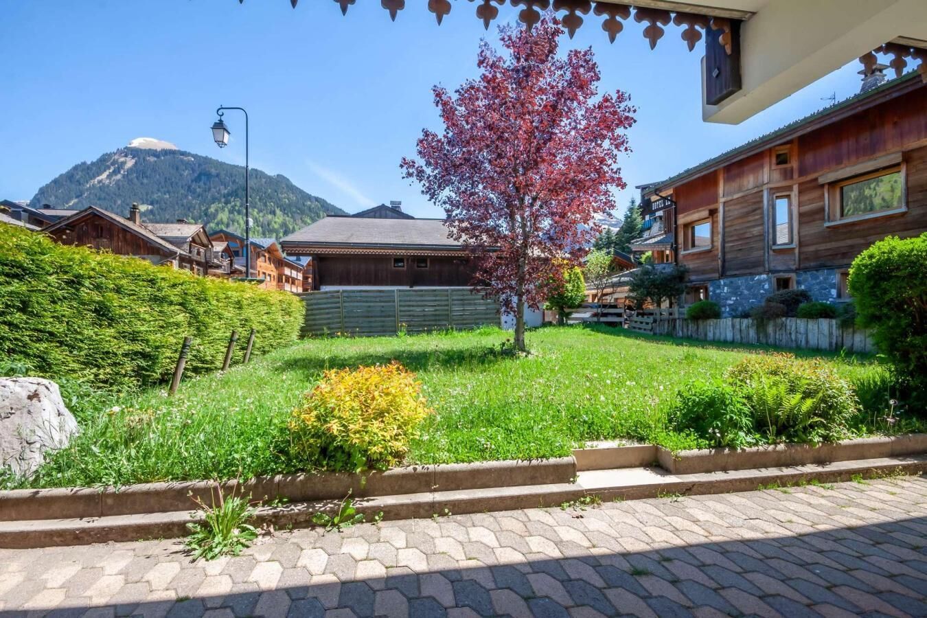 A hotel with a wooden facade, a well-maintained garden, and a mountain in the background.