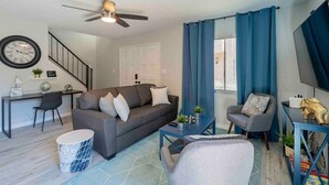 A modern living room with a grey sofa, a coffee table, a TV stand, and a ceiling fan.