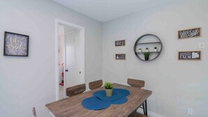 A dining area with a wooden table, four chairs, and a wall-mounted shelf with plants.