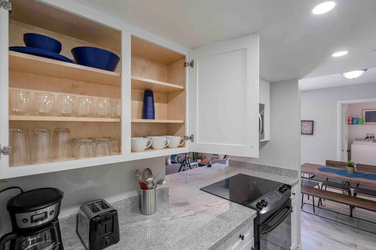A modern kitchen with white cabinets, a built-in stove, and a dining area with a table and benches.