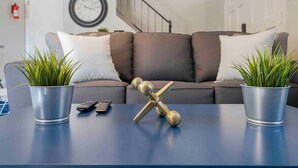 A modern living room with a sofa, two potted plants, a decorative metal sculpture, and a clock on the wall.