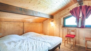 A wooden cabin room with a bed, a chair, and a window with curtains. - 100m from ski slopes, 1st floor, balcony, parking, tv, ski locker, 40m², Morzine (Morzine)