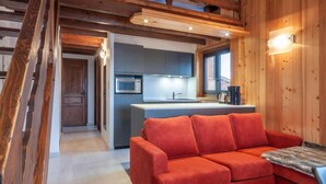 A modern kitchen with a microwave, sink, and wooden cabinets. There is a red sofa and a fur throw on a wooden table. - 100m from ski slopes, 1st floor, balcony, parking, tv, ski locker, 40m², Morzine (Morzine)