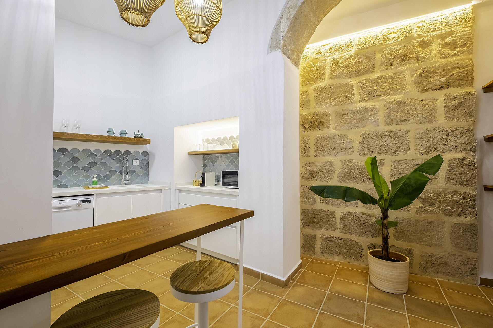 Une cuisine moderne avec des meubles blancs, un banc en bois et une plante en pot.