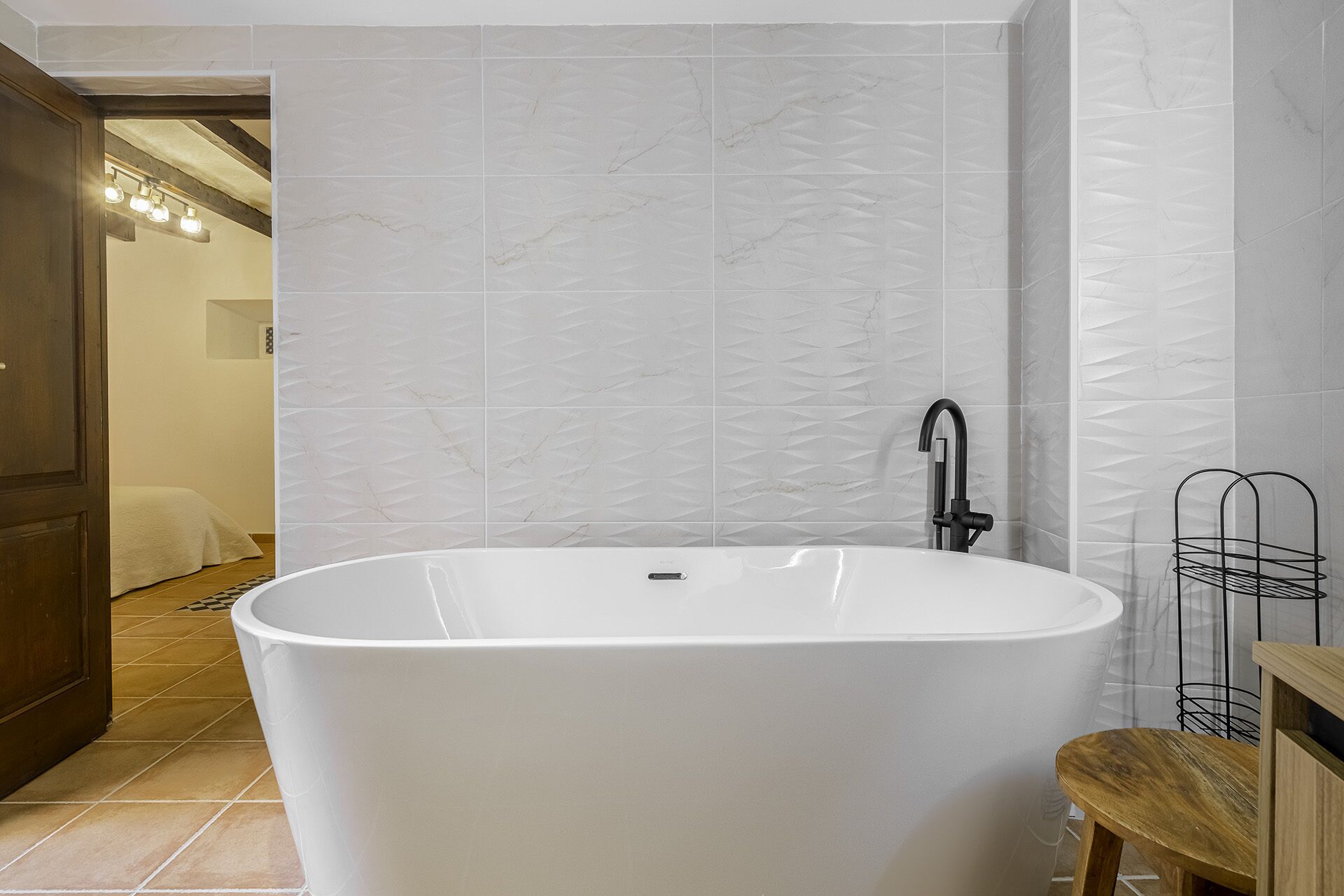 Un baño moderno con una bañera independiente, un grifo negro y un taburete de madera.