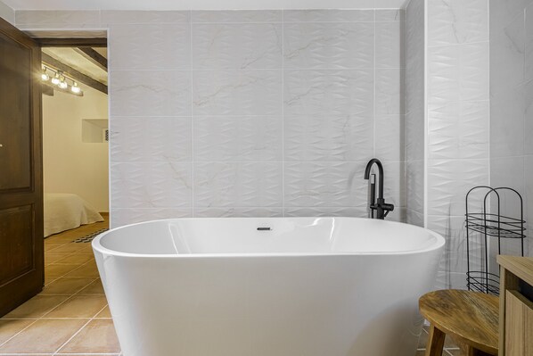 A modern bathroom with a freestanding bathtub, a black faucet, and a wooden stool. - Preciosa Casa Tradicional en el Centro de Jávea (Xàbia)