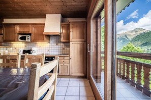 Un intérieur en bois comprenant une cuisine, une table à manger, des chaises et une vue sur un paysage montagneux, visible à travers une porte vitrée.