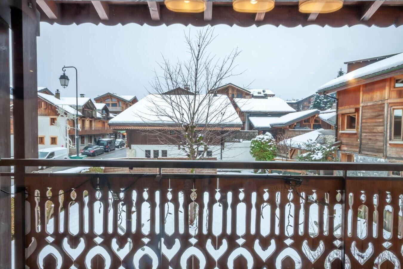En balkong med ett dekorativt metallräcke som vetter ut mot en snötäckt by med traditionella trähus.
