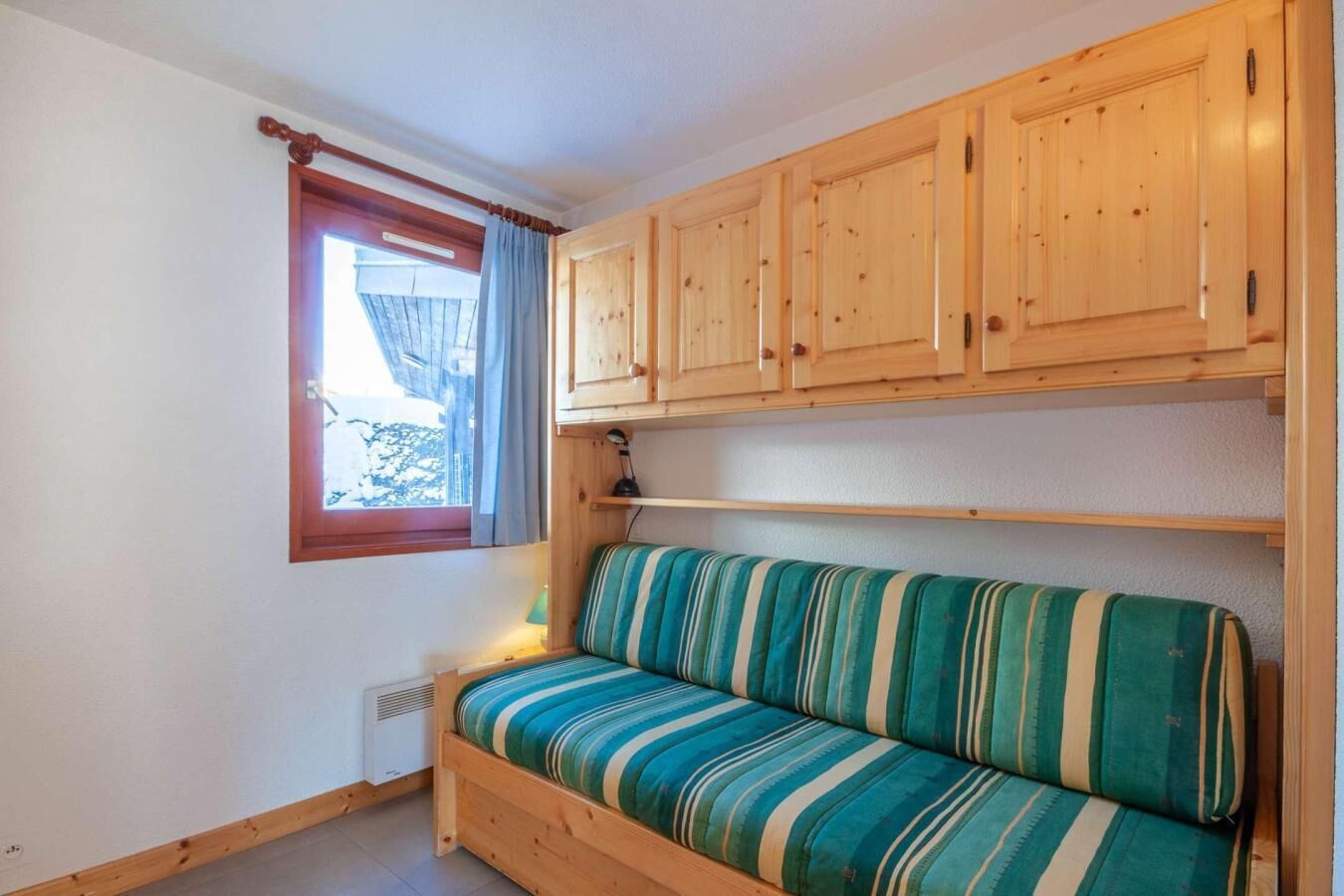 A cozy room with a wooden sofa, a window with curtains, and wooden cabinets.