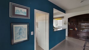 Un couloir aux murs de couleur turquoise, orné de tableaux encadrés, avec une porte blanche, un miroir et un meuble en bois.