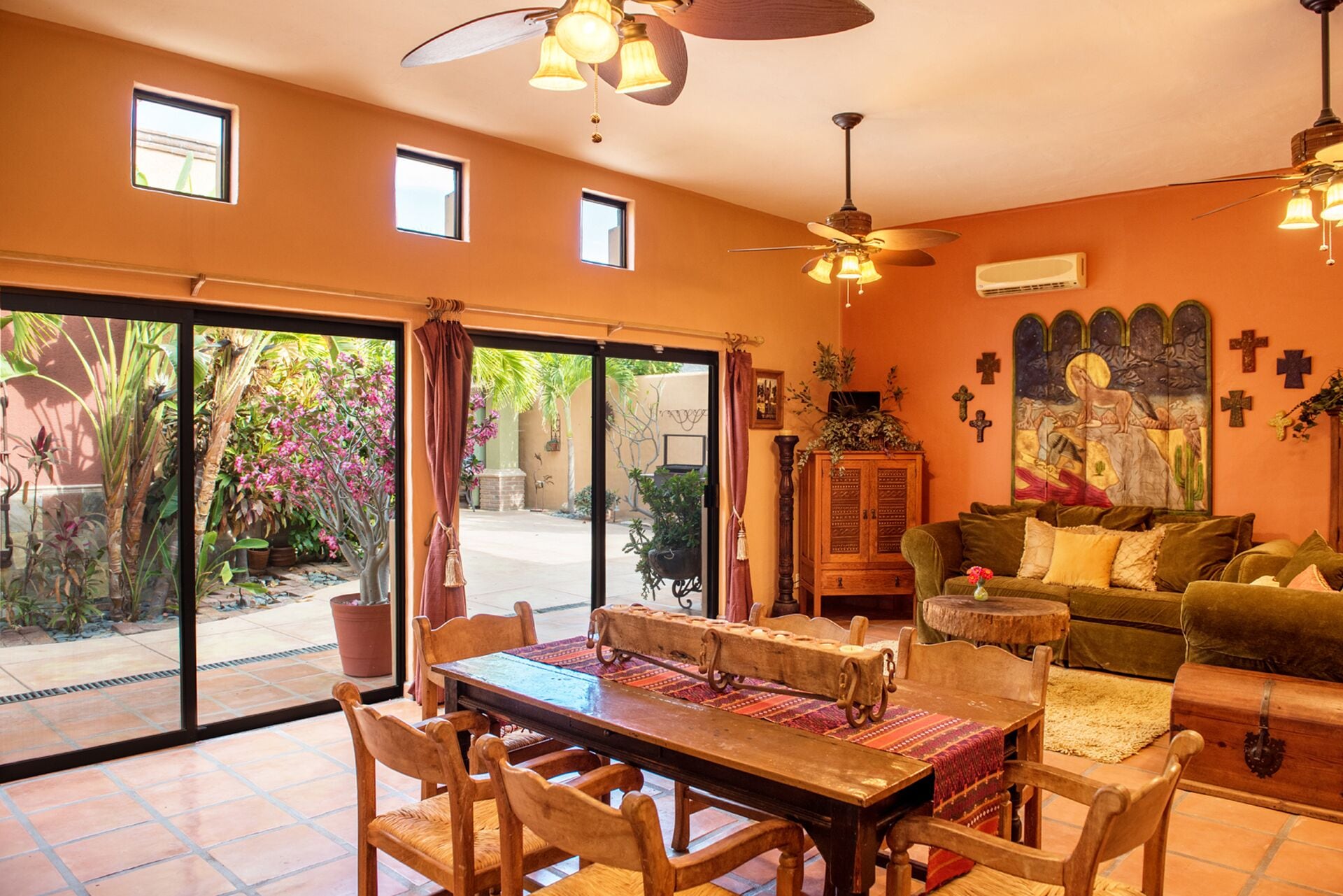 Un vaste salon doté d’une grande porte-fenêtre coulissante donnant sur un patio, d’une table à manger en bois avec des chaises, d’un canapé vert et d’un ventilateur de plafond.