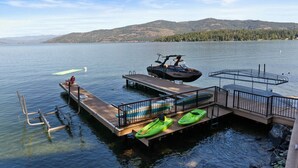 Un muelle junto al lago con kayaks, un bote y un jet ski.