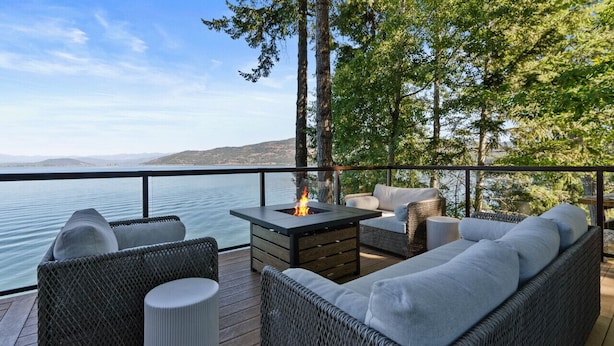 Una terraza con mobiliario de mimbre, un hogar a leña y vistas al lago.