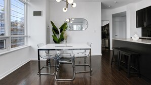 Une cuisine moderne avec un plan de travail noir, une table à manger blanche et des chaises transparentes, ainsi qu’un luminaire suspendu.