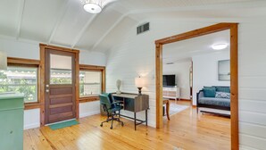 A spacious room with wooden flooring, a desk with a chair, a sofa, and a large window. - Mount Dora Home: Private Pool & Tropical Bar! (Mt Dora)