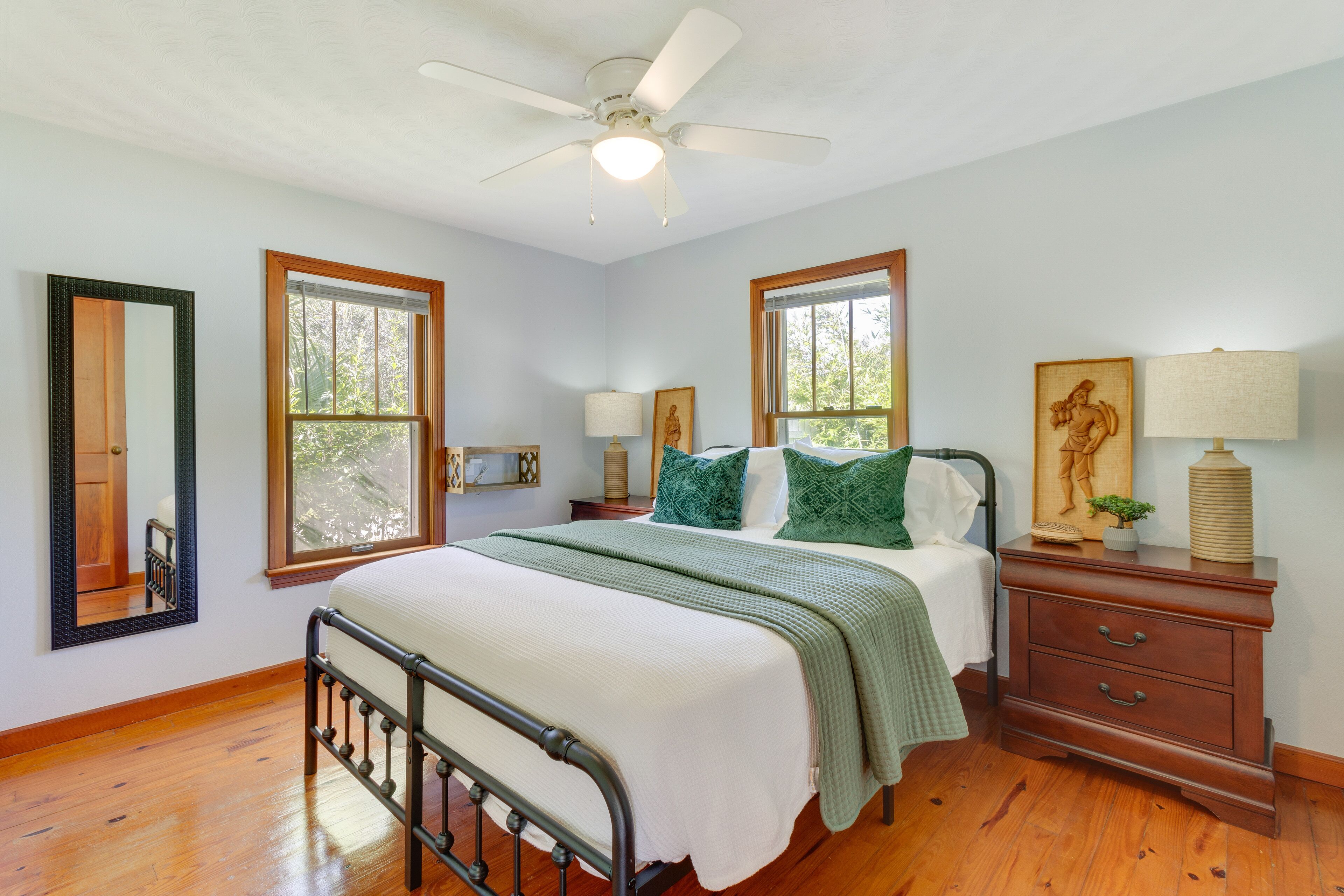 A bedroom with a bed, two windows, a nightstand, a dresser, a ceiling fan, and a mirror.