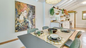 A dining area with a large painting, a modern kitchen in the background, and a dining table set with plates and glasses. - Mount Dora Home: Private Pool & Tropical Bar! (Mt Dora)