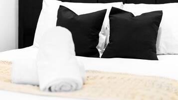 Una cama bien hecha con almohadas blancas y negras, una toalla blanca enrollada y una manta beige.
