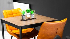 A dining area with a wooden table, two potted plants, and two yellow chairs.