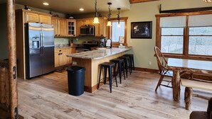 Une cuisine dotée de meubles en bois, d’appareils électroménagers en acier inoxydable, d’un plan de travail en granit et d’un coin repas avec une table et des chaises en bois.