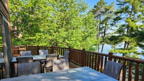 Une terrasse extérieure avec des tables et des chaises, entourée d’arbres et donnant sur une étendue d’eau.