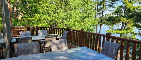 An outdoor deck with tables and chairs, surrounded by trees and overlooking a body of water.