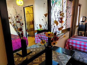 A room with a bed, a table with a vase of flowers, a mirror reflecting the room, and a window with a view of the outside. - Apartamento Céntrico Vive El Pulsar De La Ciudad (Toluca)