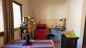Una cocina pequeña con una mesa cubierta por un mantel a cuadros, un jarrón con flores, un electrodoméstico rojo y un lavabo.