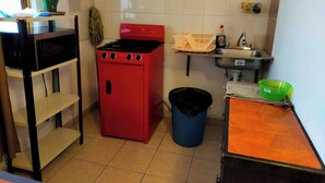 Una cocina compacta con estufa roja, un fregadero, un microondas y un cubo de basura.