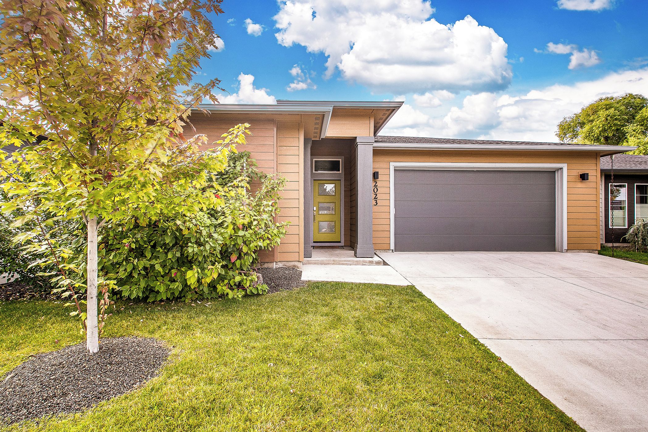 A modern two-story house with a garage, a well-maintained lawn, and mature trees.