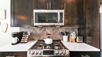 A modern kitchen with dark wooden cabinets, a stainless steel microwave, a gas stove, a coffee maker, and a toaster.