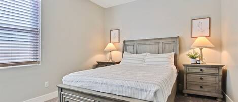 A bedroom with a bed, two nightstands, a dresser, a window with blinds, and wall art.