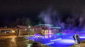 A nighttime swimming pool with a fountain, surrounded by a building with illuminated railings.