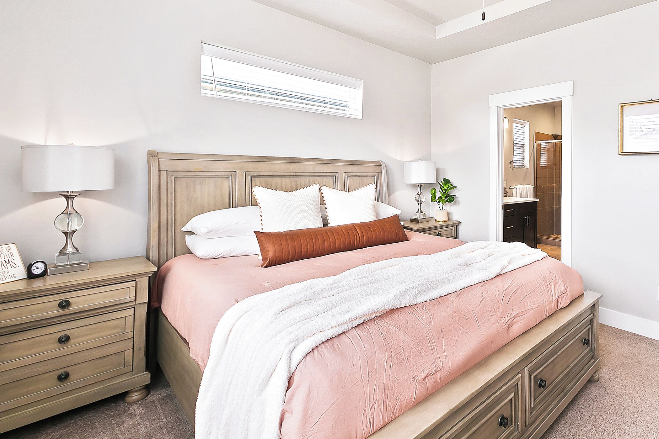 A bedroom with a bed, bedside tables, a nightstand, a lamp, a clock, a mirror, and a door leading to a bathroom.