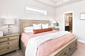 A bedroom with a bed, bedside tables, a nightstand, a lamp, a clock, a mirror, and a door leading to a bathroom.