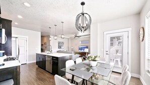A modern kitchen with a central island, a dining area with a glass table, and a living space with a sofa and TV.