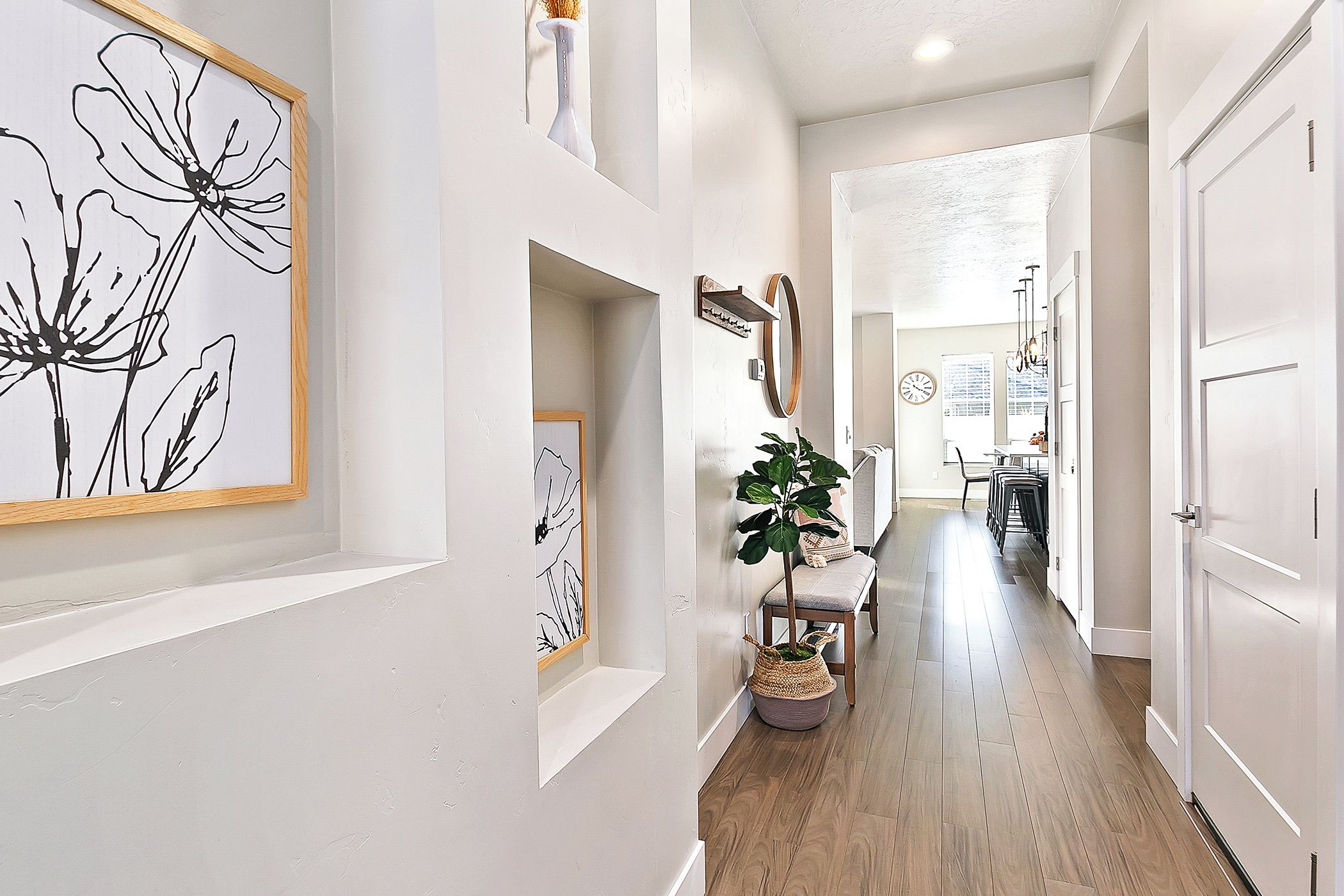 A hallway with a wooden floor, white walls, and a dining area in the distance.