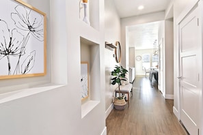 A hallway with a wooden floor, a potted plant, a framed artwork, and a mirror on the wall. - Top Rated • Spotless • Prime Central Location • Where Guests Return (Meridian)