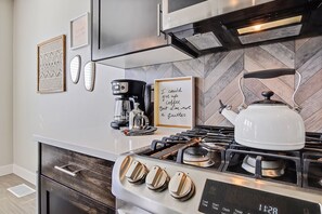 A modern kitchen with a gas stove, a coffee maker, and a kettle. - Top Rated • Spotless • Prime Central Location • Where Guests Return (Meridian)