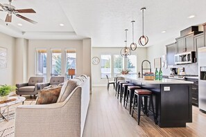 A modern kitchen with a central island, bar stools, and a dining area with a sofa and chairs.