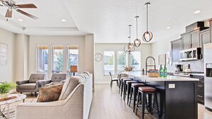 A modern kitchen with a central island, bar stools, and a dining area with a sofa and chairs.
