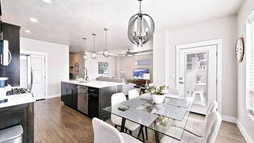 A modern kitchen with a central island, a dining area with a glass table, and a living space with a sofa and TV.