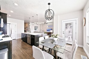 A modern kitchen with a central island, a dining area with a glass table, and a living space with a sofa and TV. - Top Rated • Spotless • Prime Central Location • Where Guests Return (Meridian)