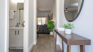 A hallway with a wooden floor, a white door leading to a bathroom, a dining area with a table and chairs, and a large mirror on the wall. - Newly Renovated Townhouse! (Davenport)