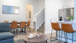 A modern living room with a sofa, dining table, chairs, and a kitchen area with a refrigerator and bar stools. - Newly Renovated Townhouse! (Davenport)