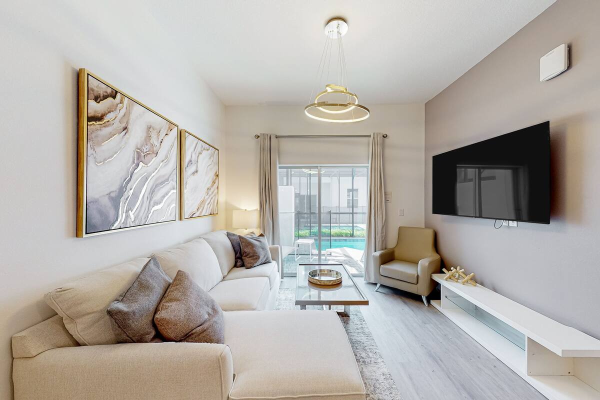 A modern living room with a sofa, armchairs, a coffee table, and a flat-screen TV mounted on the wall.