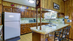 A kitchen with wooden cabinets, a refrigerator, a marble countertop, and bar stools. - Vintage Chipley Getaway on Large Private Property (Chipley)