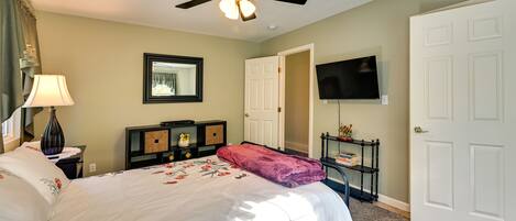 A hotel room with a bed, ceiling fan, TV, and a door.
